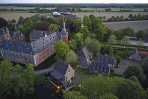 An aerial view of a historic estate with a prominent castle-like building, a church with a tall spire, and surrounding lush greenery. - Schloss Wissen Hotellerie (Weeze)