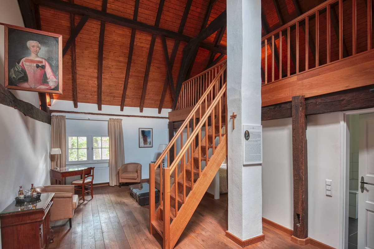 A spacious room with wooden floors, a staircase, a dining area with a table and chairs, and a painting on the wall.