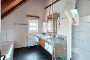 A modern bathroom with a large window, a glass shower enclosure, a white bathtub, and a granite countertop sink. - Schloss Wissen Hotellerie (Weeze)