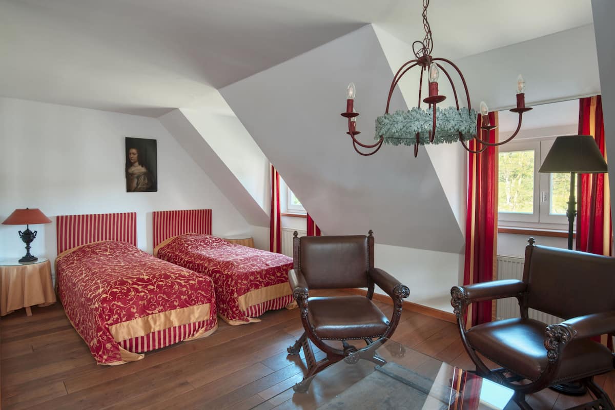A bedroom with two beds, a chandelier, and a chair.