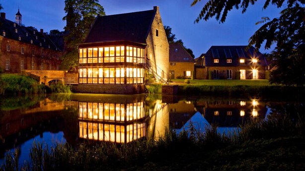 A historic building with large windows and a reflection in the water.