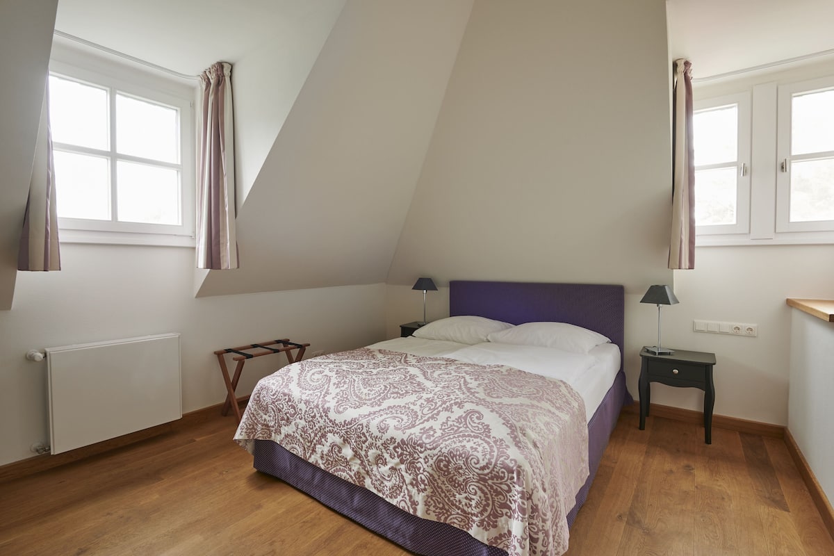 A bedroom with a bed, a nightstand, a radiator, and a window with curtains.