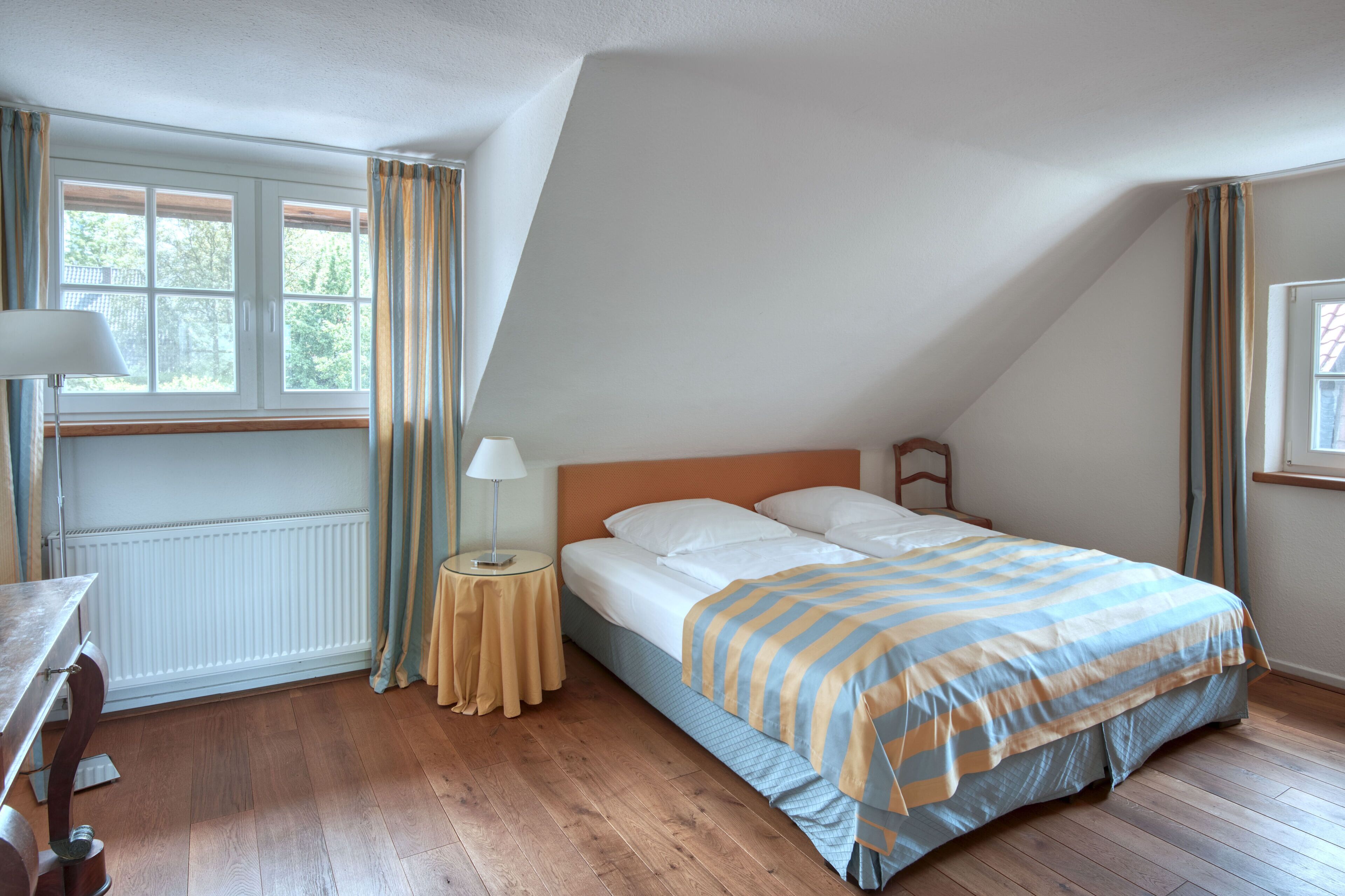Un dormitorio con cama, mesita de noche, lámpara, ventana y radiador.