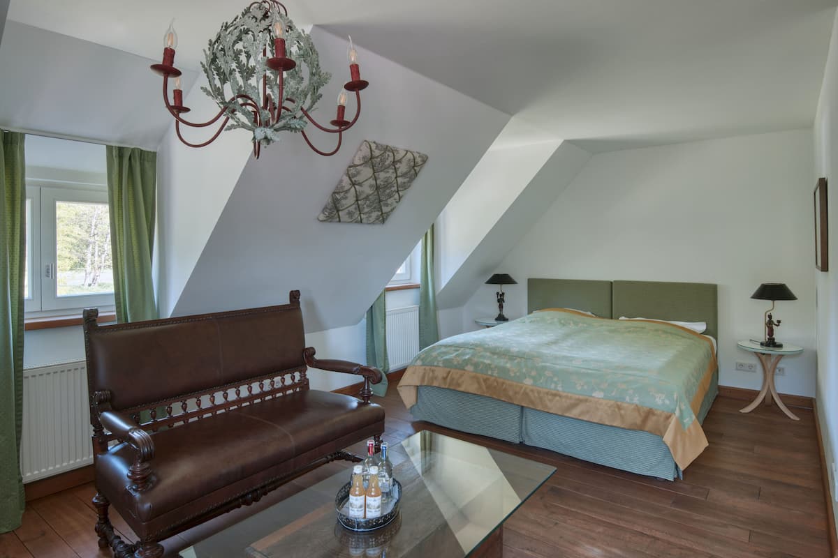 A bedroom with a large bed, a wooden bench, a chandelier, and a window with curtains.