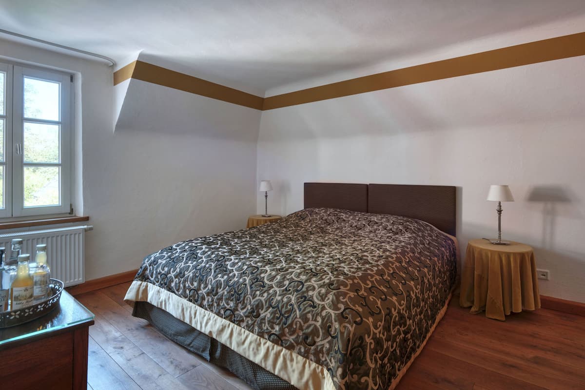 A bedroom with a large bed, two bedside tables, a window, and a radiator.