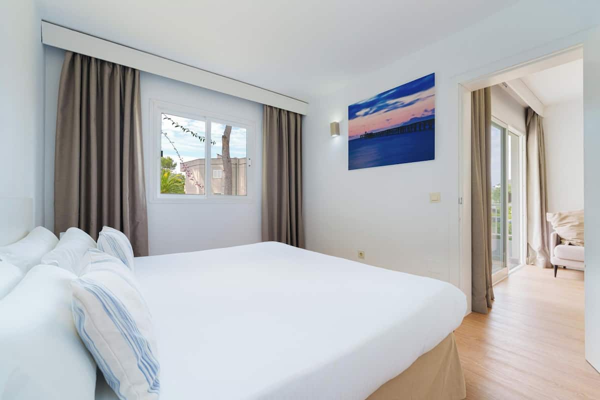 Hotelkamer met een groot bed, een raam met gordijnen, een schilderij aan de muur en uitzicht op het omliggende landschap.