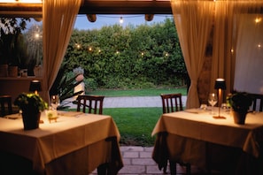 An outdoor dining area with tables, chairs, string lights, and a view of a garden. - Casina Dei Preti (Conversano)
