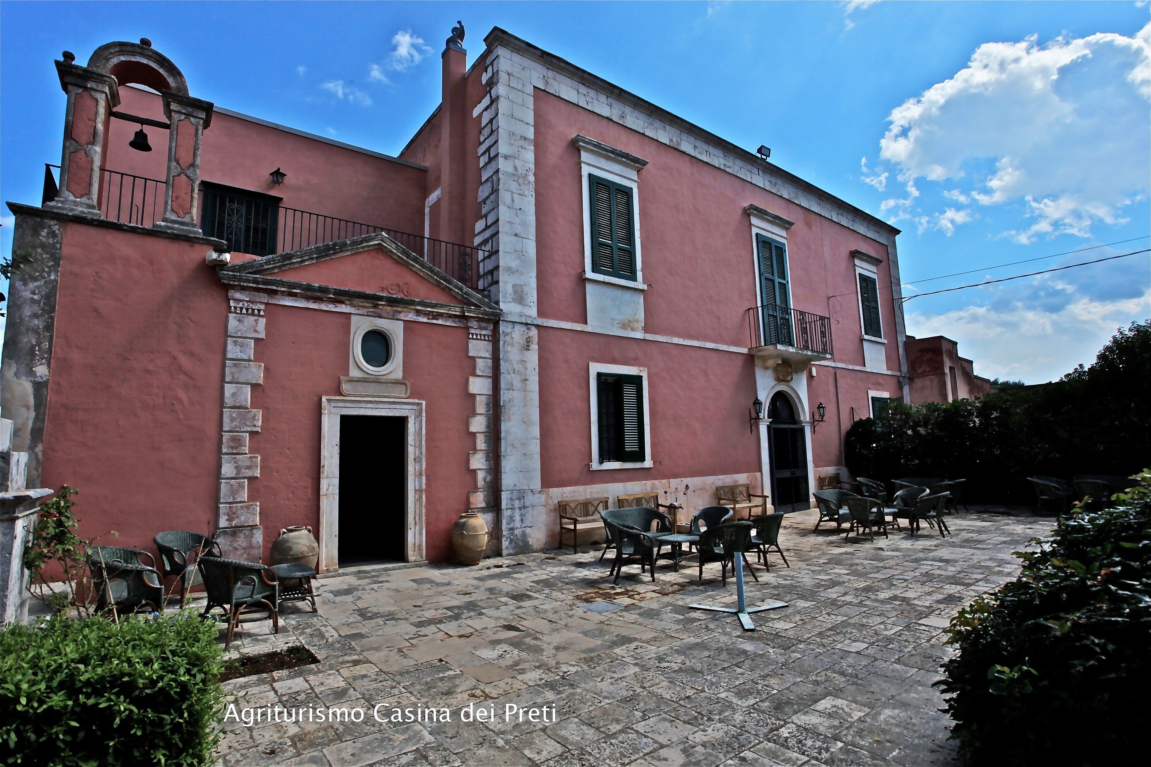 A historic building with a red facade, a bell tower, and a courtyard with outdoor seating.