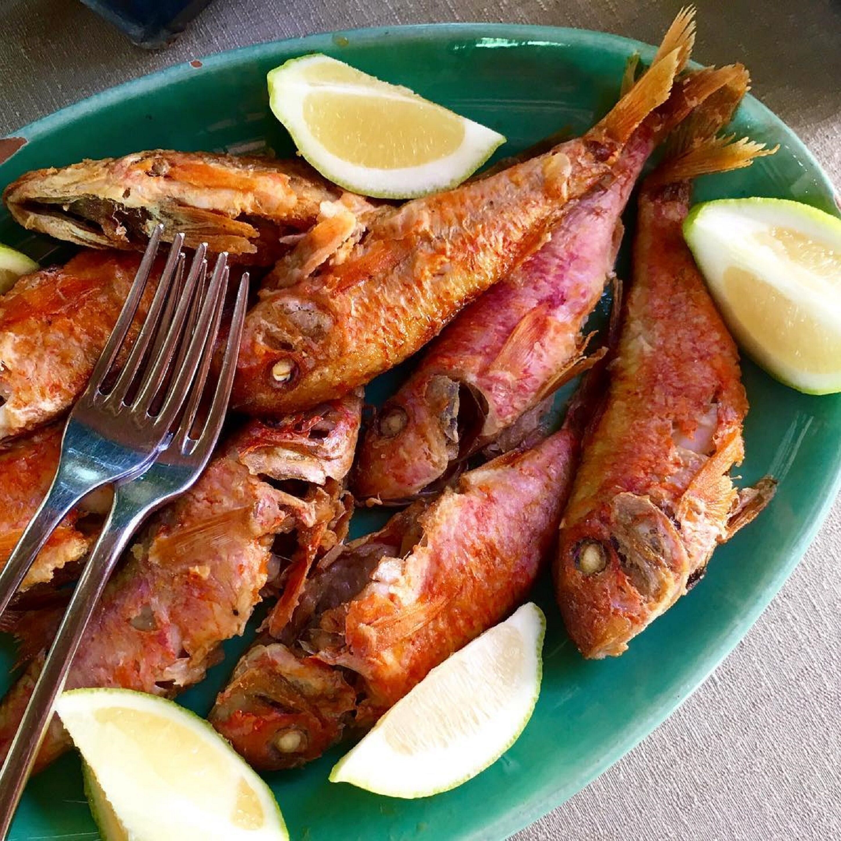 A plate of fried fish with lemon wedges.