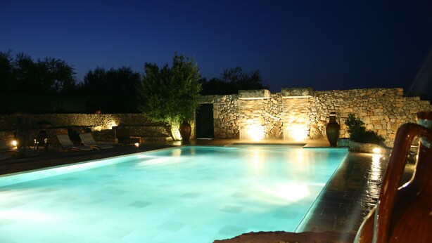 A swimming pool with stone walls and lounge chairs, surrounded by trees and a stone wall. - Casina Dei Preti (Conversano)