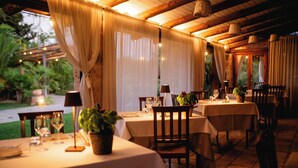 An outdoor dining area with tables set for two, featuring white tablecloths, wooden chairs, and potted plants. - Casina Dei Preti (Conversano)