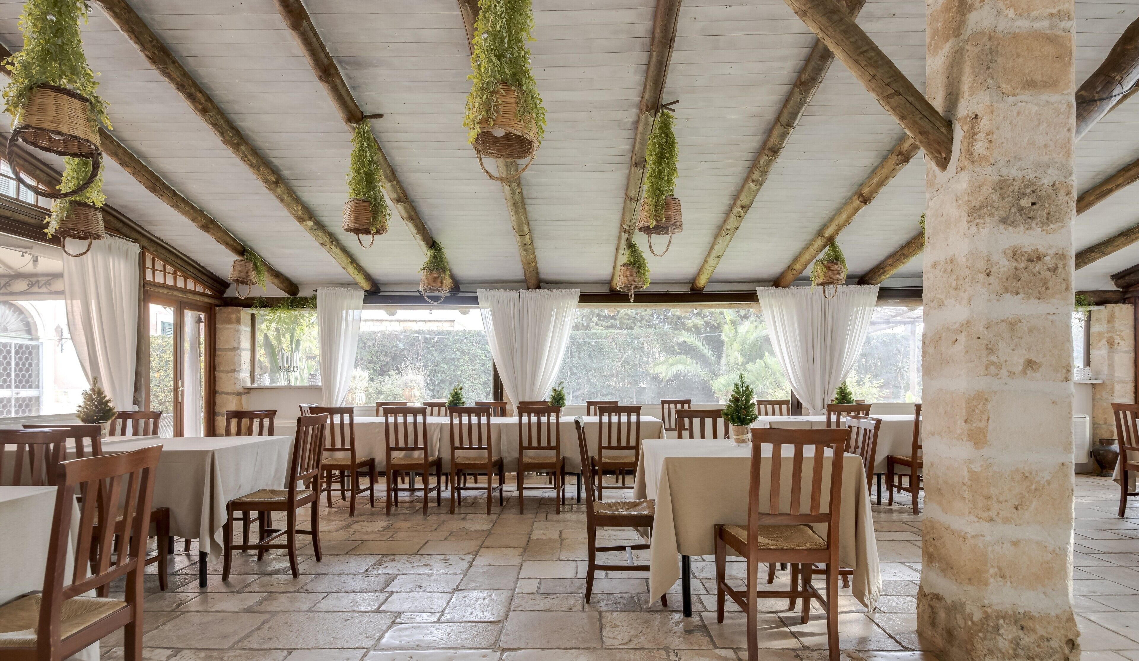 A restaurant with wooden tables and chairs, hanging plants, and a stone floor.