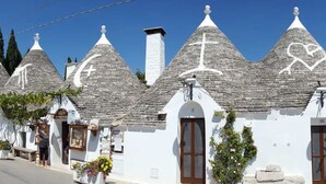 A row of white buildings with conical roofs, each with a wooden door and small windows. - Casina Dei Preti (Conversano)
