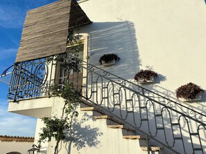 A building with a white facade, a wooden sloped roof, and a metal staircase with ornate balustrades. - Casina Dei Preti (Conversano)