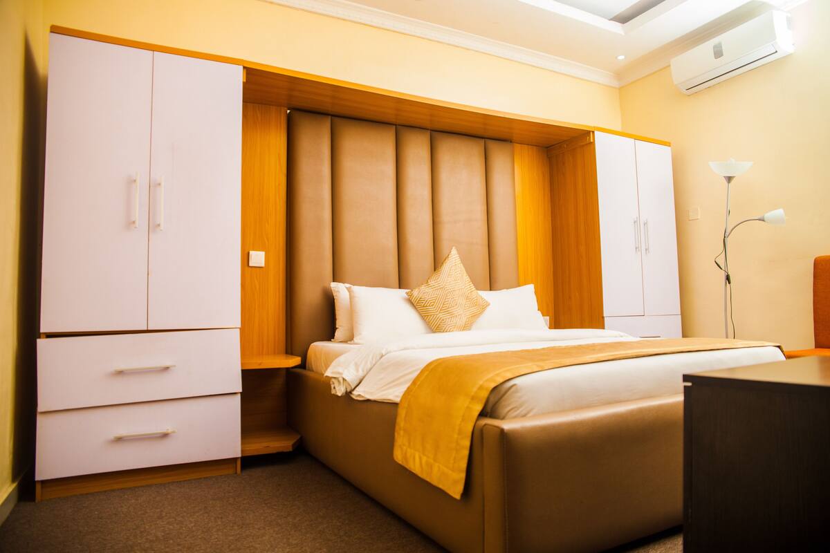 A bedroom with a bed, wooden headboard, white wardrobe, and a desk.