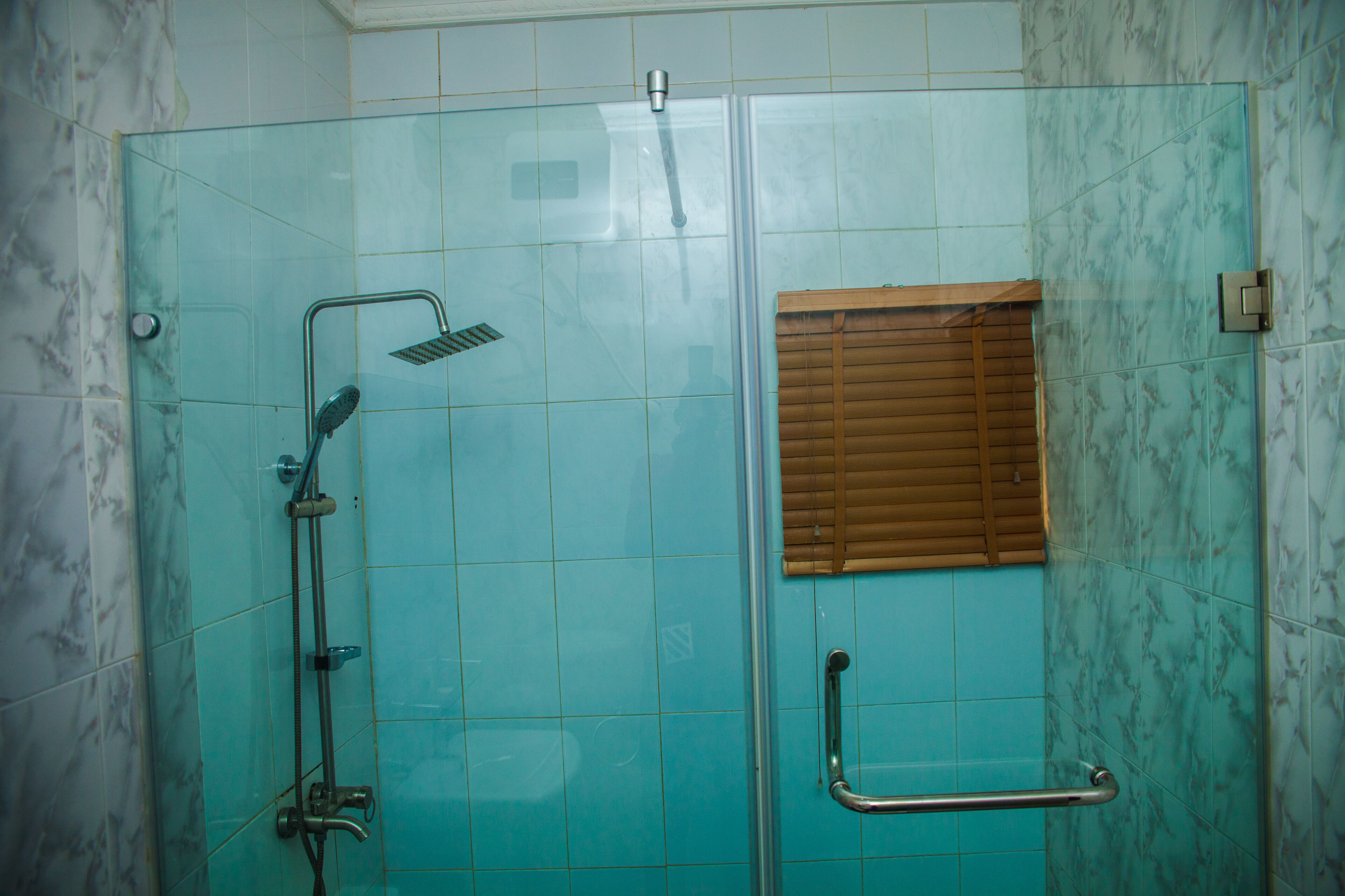 A glass-enclosed shower with a handheld showerhead and a handheld faucet.