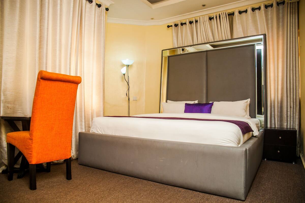 A hotel room with a bed, a chair, a nightstand, and a lamp.