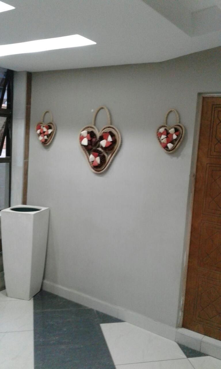 Un couloir avec une poubelle blanche, une porte en bois et trois décorations murales en forme de cœur.
