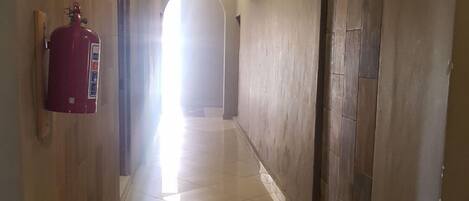 A corridor with a fire extinguisher mounted on the wall, a tiled floor, and an arched doorway at the end.