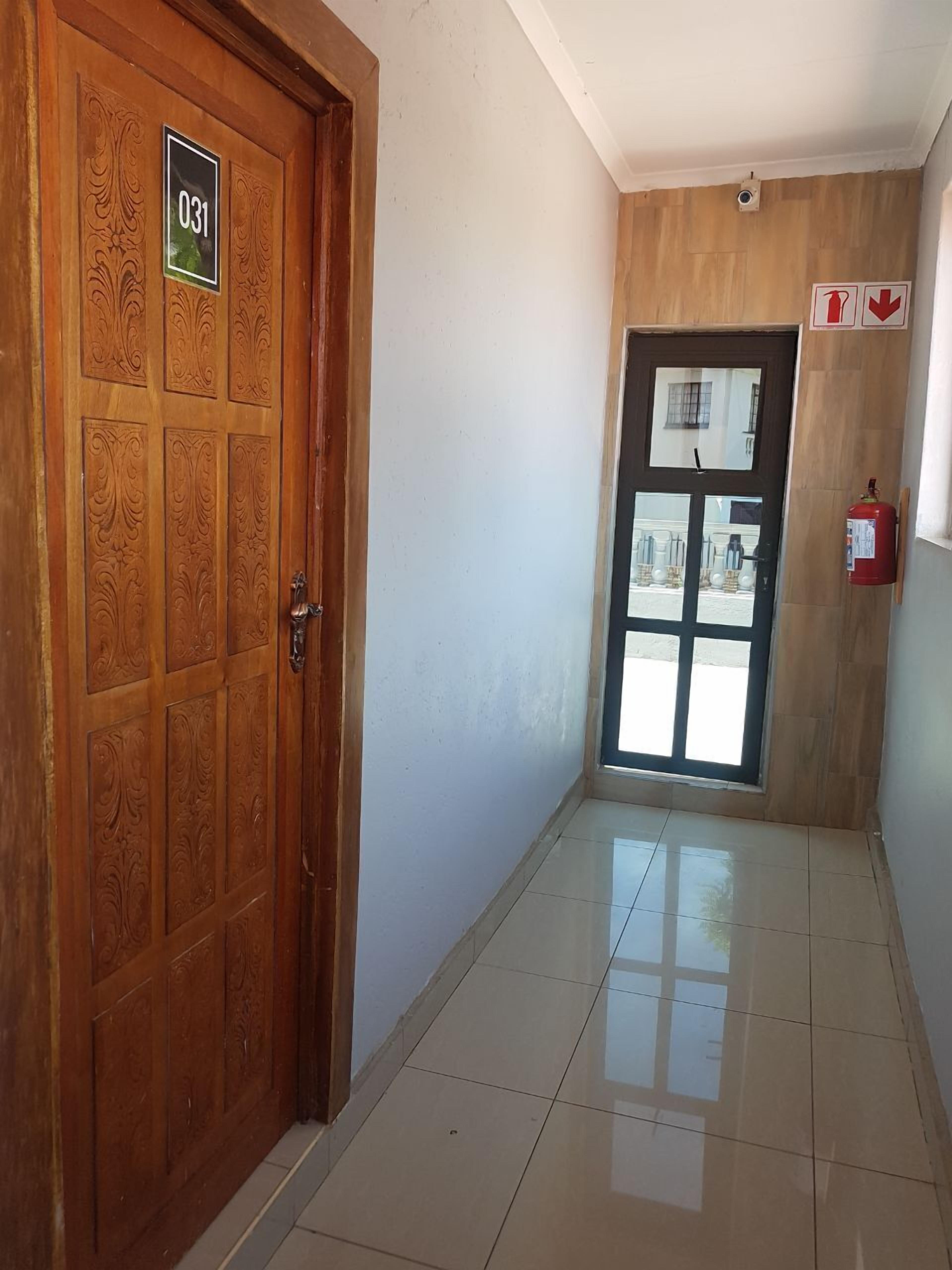 Un pasillo con una puerta de madera marcada con el número "031", un extintor y una ventana que da a vistas exteriores.