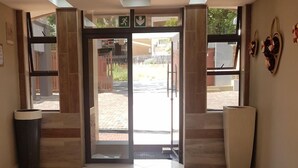 Vestíbulo de hotel con puerta de cristal, un cesto de basura y un adorno colgado en la pared.