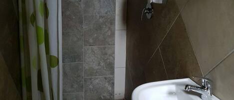 Un baño con ducha, lavamanos y un perchero para toallas.
