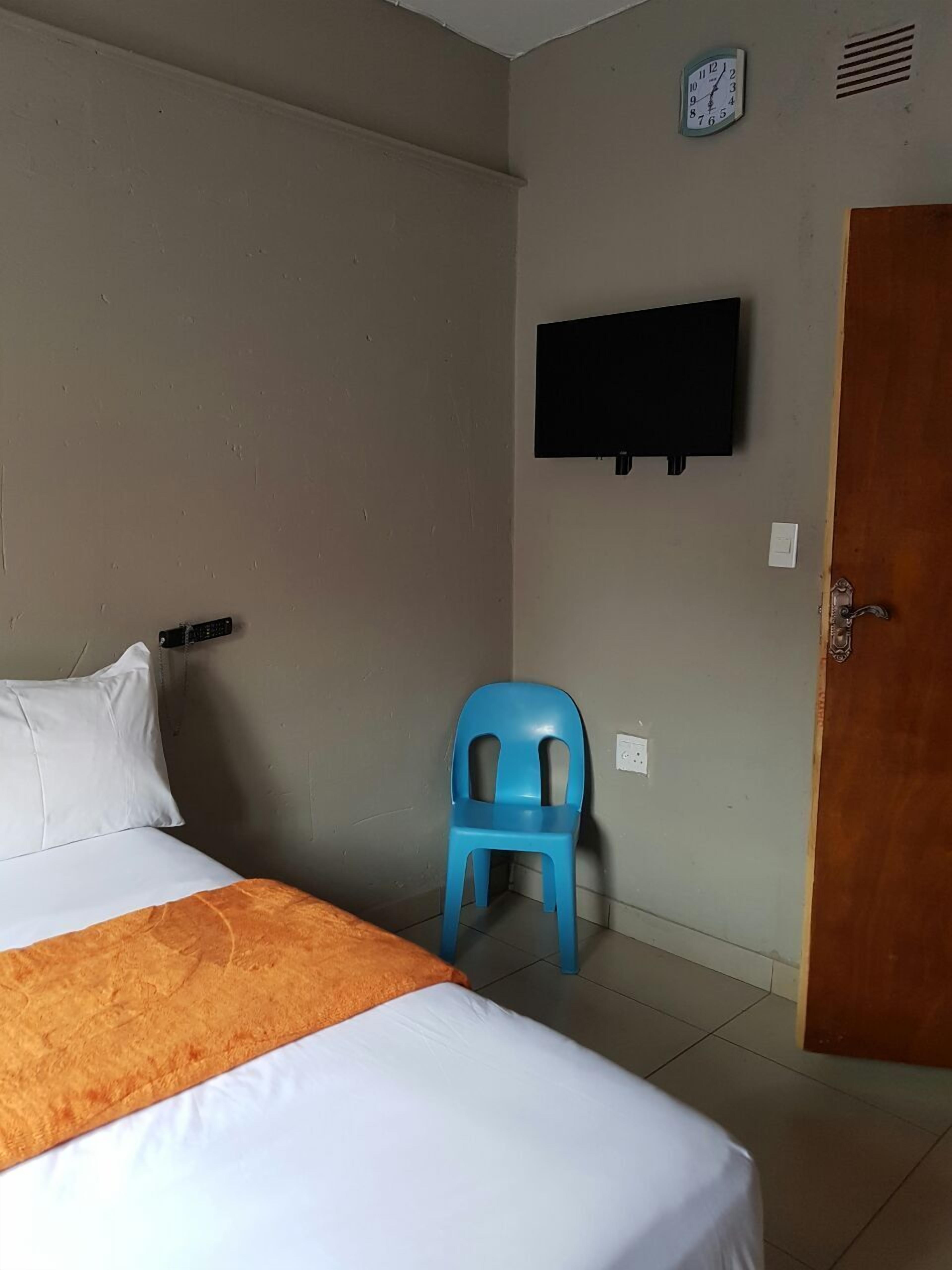 A bedroom with a bed, a blue chair, a wall-mounted TV, and a door.