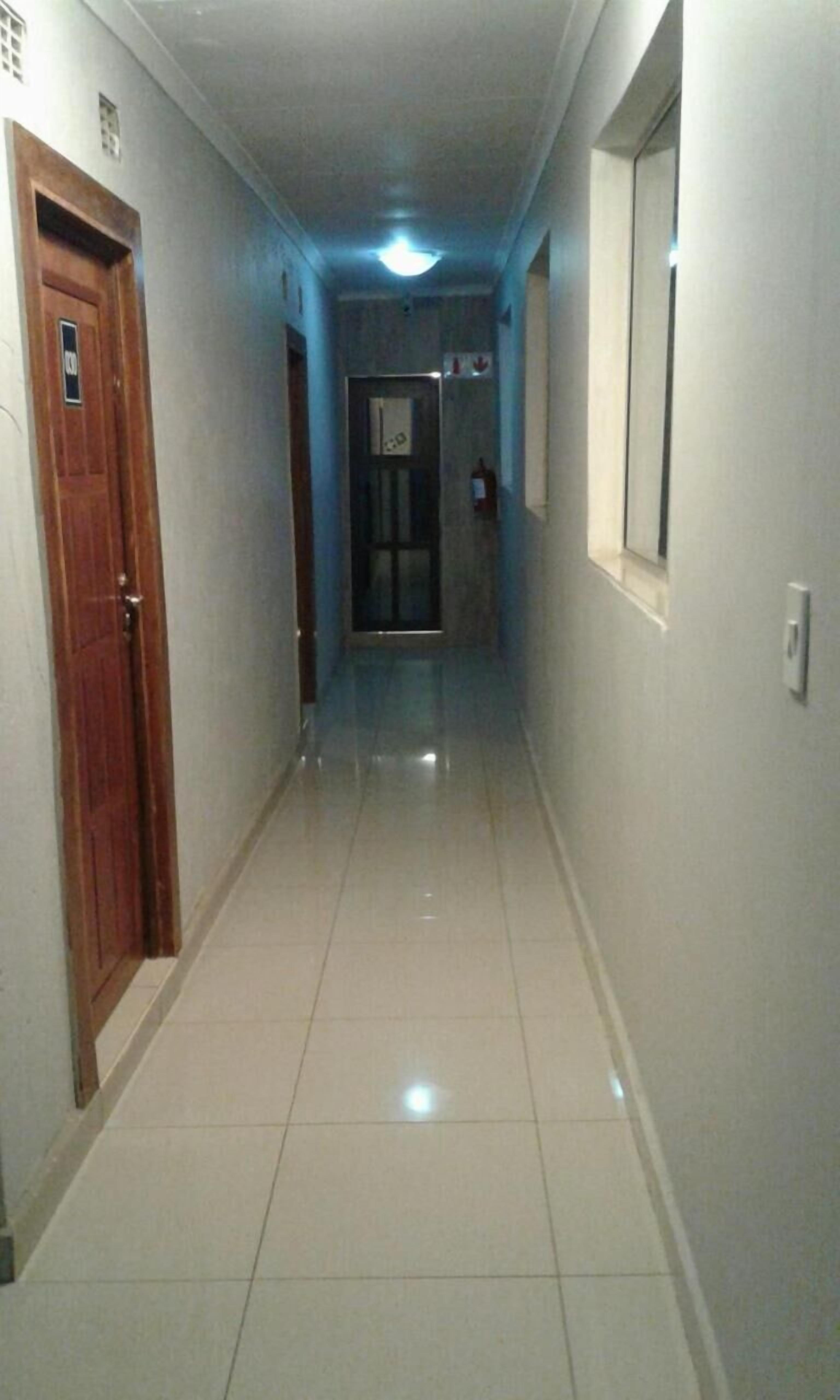 Un pasillo con una puerta de madera a la izquierda, una ventana a la derecha y otra puerta al final.
