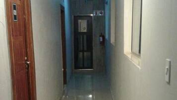 Un pasillo con una puerta de madera a la izquierda, una ventana a la derecha y otra puerta al final.