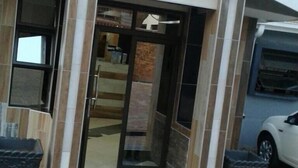 Una entrada de edificio con puerta de cristal, un felpudo verde pequeño y un coche blanco estacionado cerca.