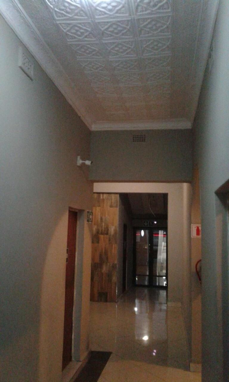 A hallway with a patterned ceiling, a door on the left, and a fire extinguisher on the right.