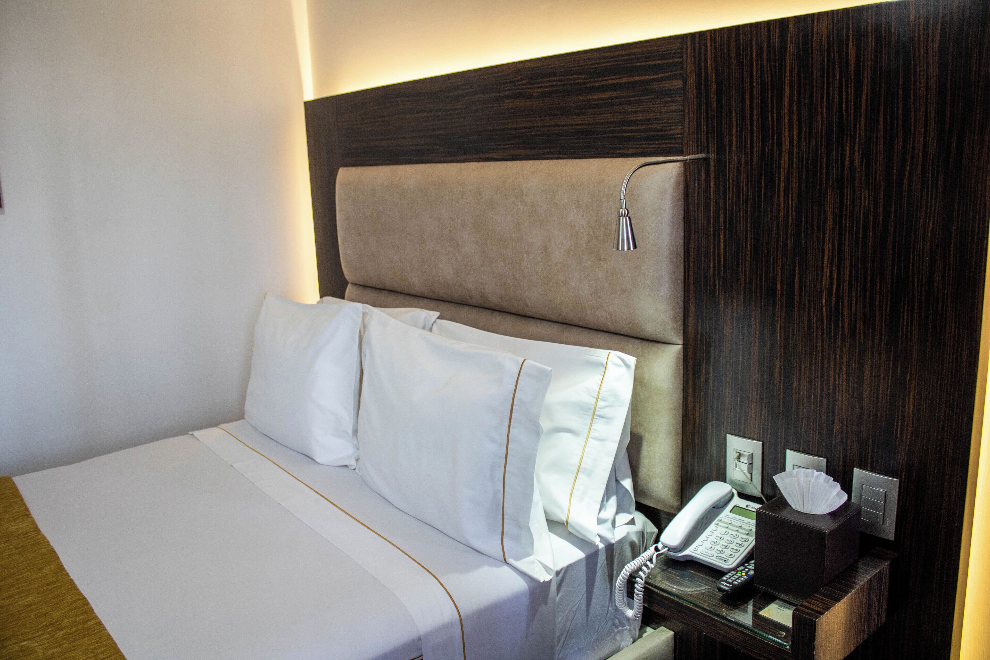 Une chambre d’hôtel avec un lit, une table de chevet avec un téléphone, une lampe et une boîte de mouchoirs.