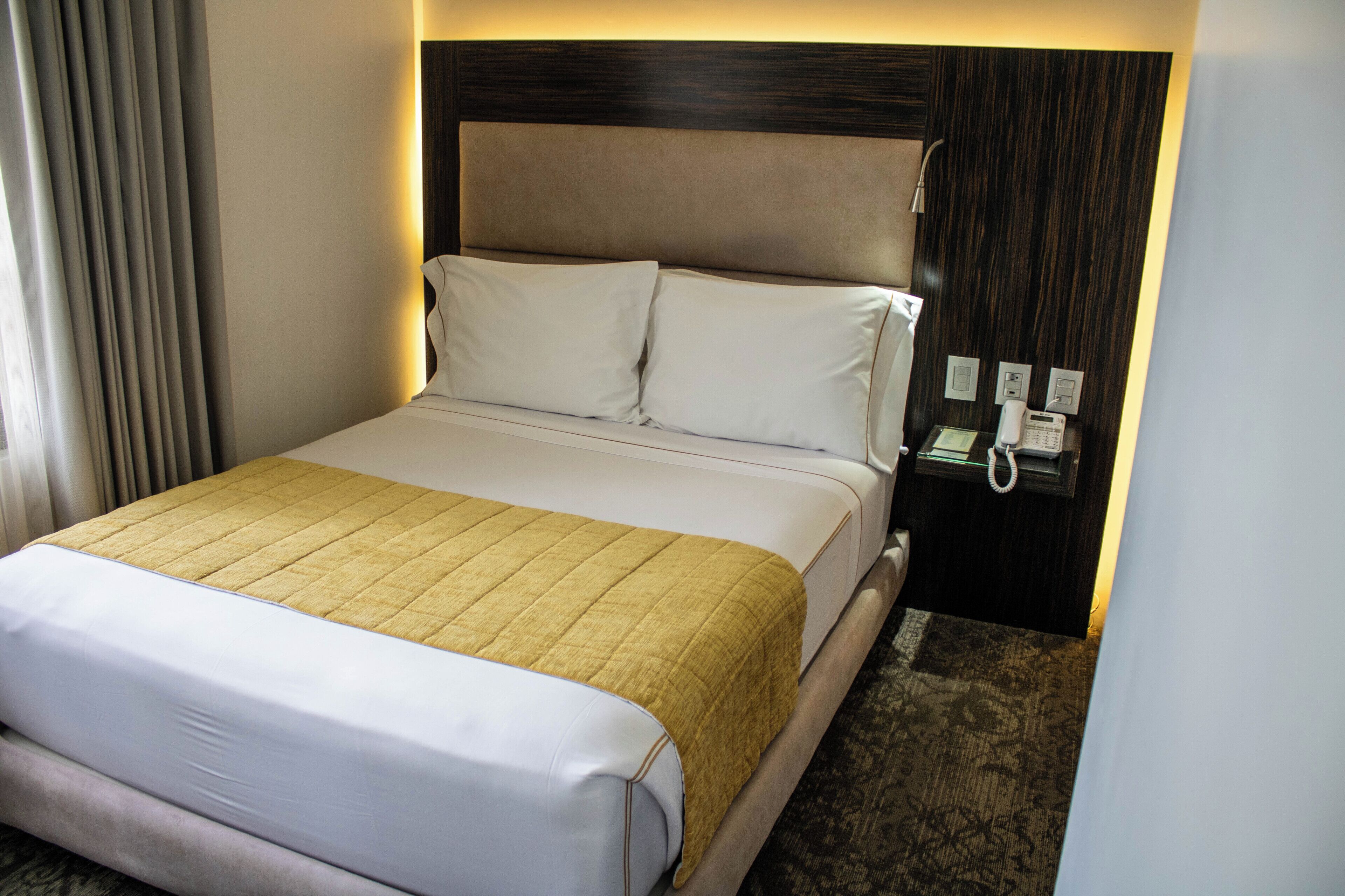 Habitación de hotel con cama, mesita de noche y cabecero.
