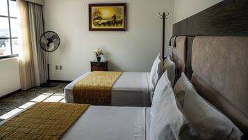 Habitación de hotel con dos camas, un ventilador, un cuadro en la pared y una ventana con cortinas.