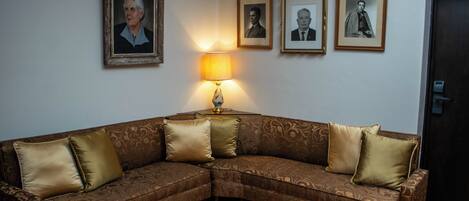A corner living room with a brown patterned sofa, three framed portraits on the wall, and a table lamp.