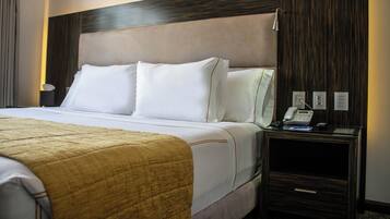 Una habitación de hotel con una cama grande, una mesita de noche con un teléfono y una mesita auxiliar.