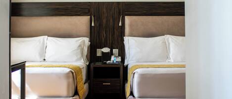 A hotel room with two beds, a wooden floor, a nightstand, and a ceiling light.