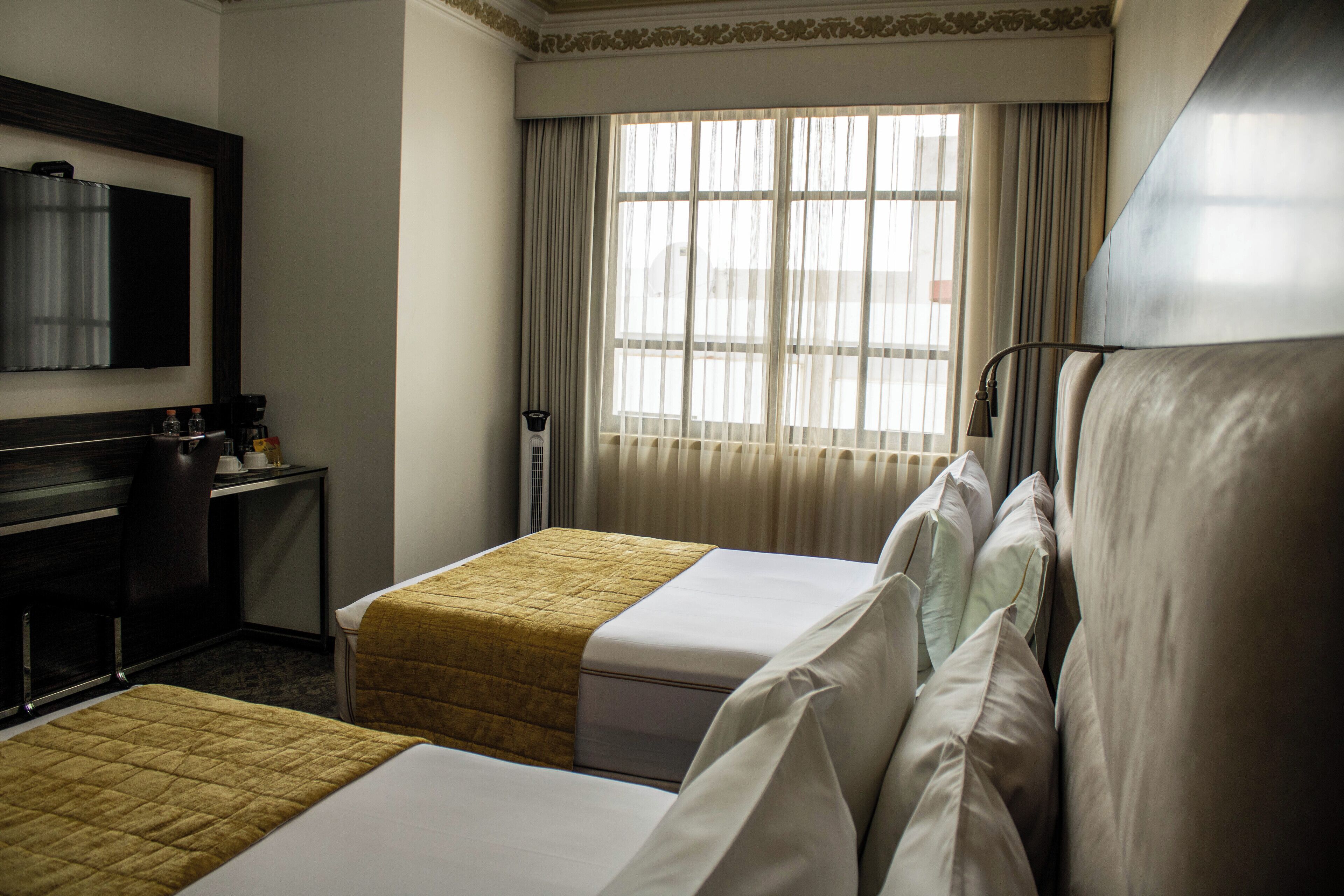 A hotel room with two beds, a desk, a chair, a television, and a window with curtains.