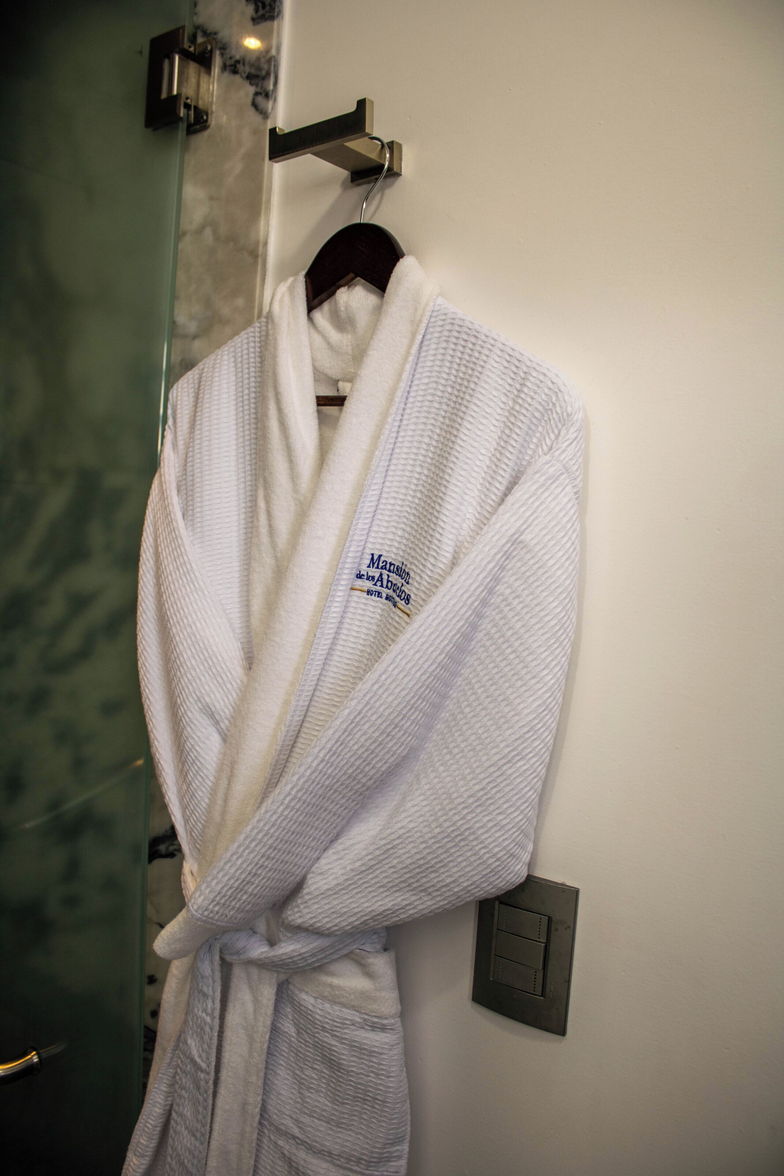 A white bathrobe hanging on a hook in a bathroom with a marble wall and a light switch.