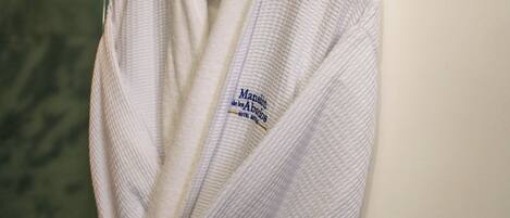 A white bathrobe hanging on a hook in a bathroom with a marble wall and a light switch.