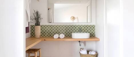 Un baño con un tocador de madera, un lavamanos blanco, un espejo y un salpicadero con diseño.