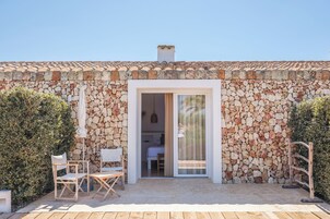 A stone-walled building with a tiled roof, a sliding glass door leading to a bedroom, and a small outdoor seating area with a table and chairs.
