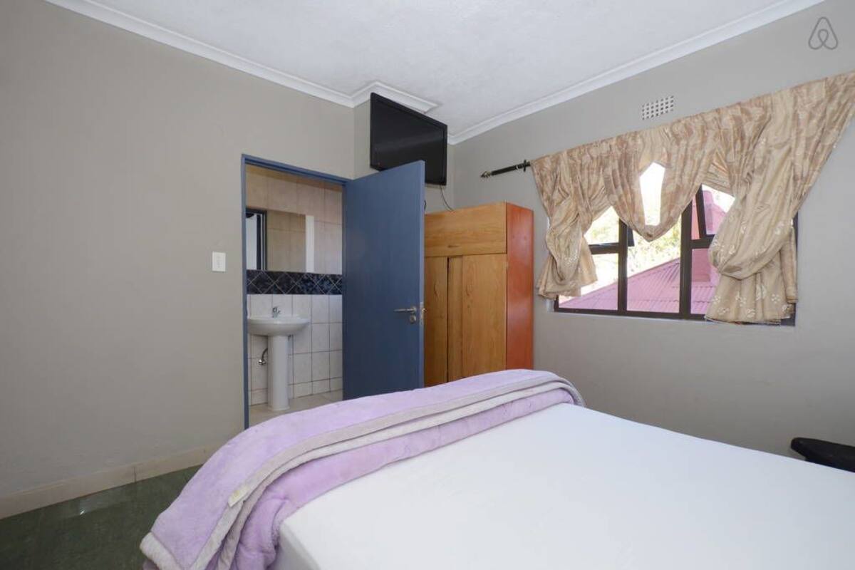 Une chambre à coucher comprenant un lit, une armoire, une fenêtre avec des rideaux, un lavabo et un miroir.