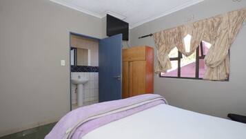 Un dormitorio con cama, armario, ventana con cortinas, lavamanos y espejo.