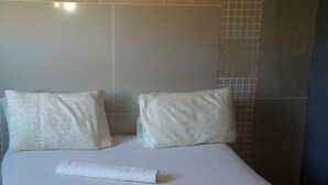 Een bed met witte beddengoed en twee kussens, een bruin hoofdbord en een betegelde muur.