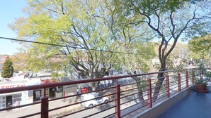 Een balkon met een rode reling met uitzicht op een straat met bomen en een gebouw met een bord waarop 