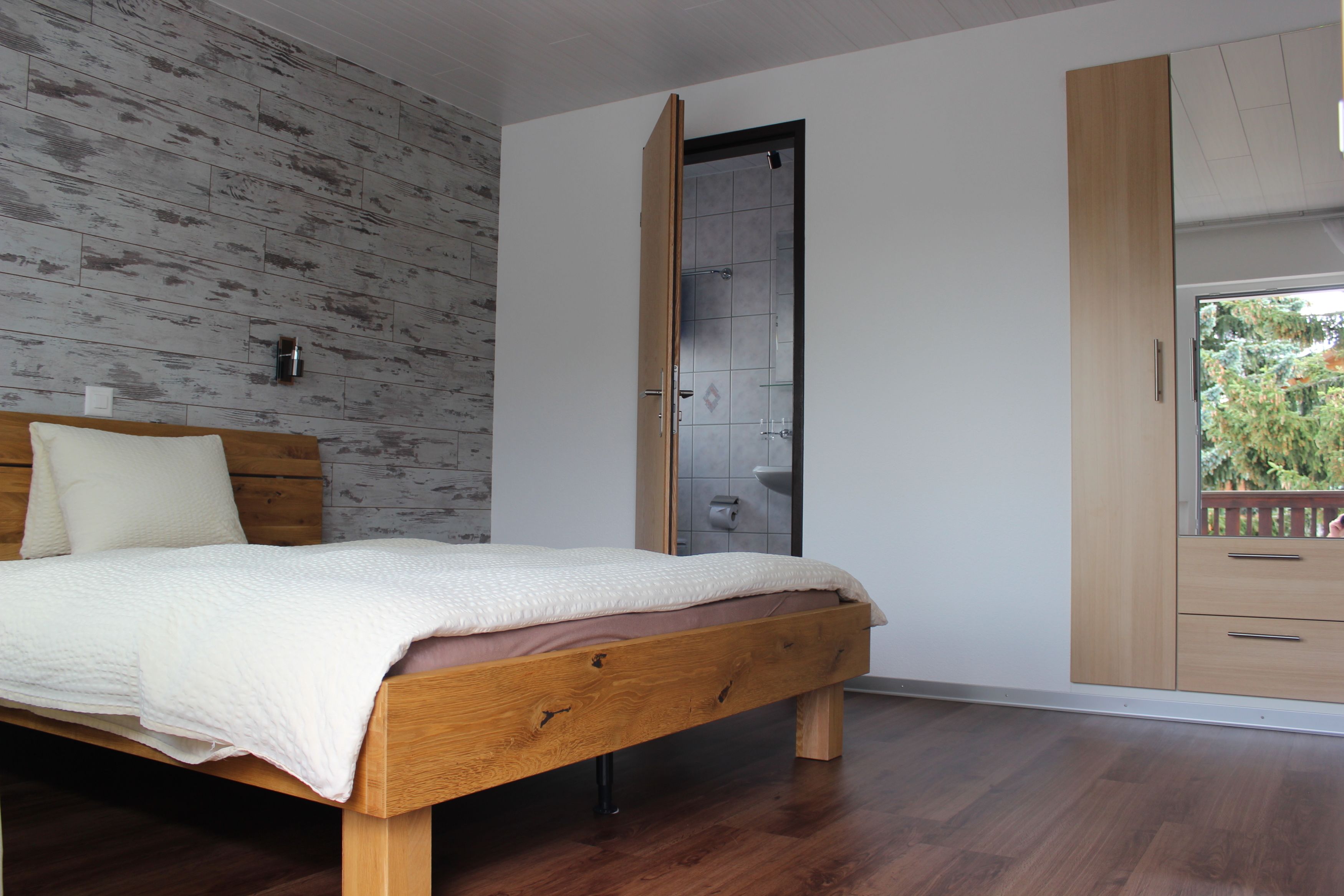 A bedroom with a wooden bed, a white wall, and a wooden wardrobe.