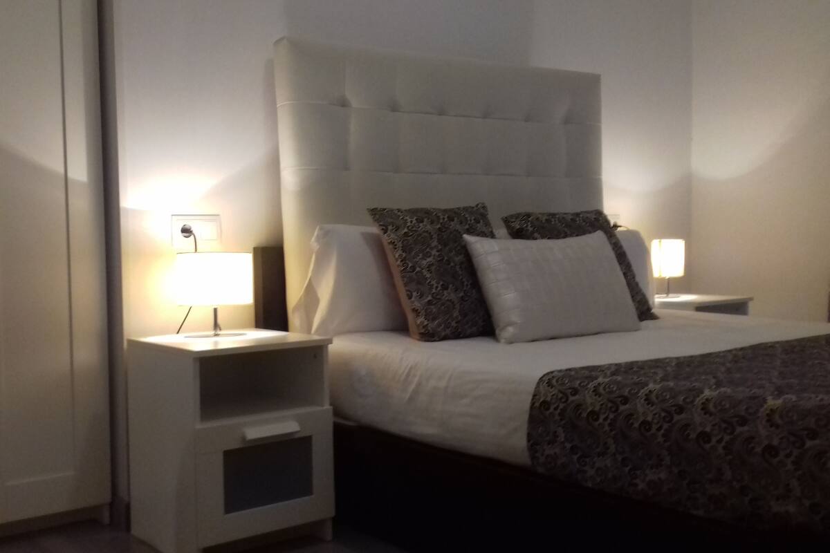 A neatly arranged bedroom with a large bed, two bedside tables, and a wardrobe.