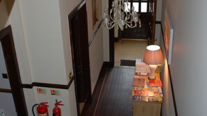 A narrow hallway with wooden flooring, a fire extinguisher, a small table with books, and a chandelier. - Westview (Perth)