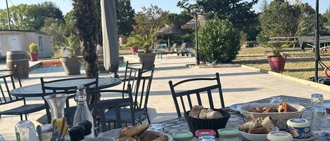An outdoor dining area with a table set for breakfast, including croissants, bread, and condiments.